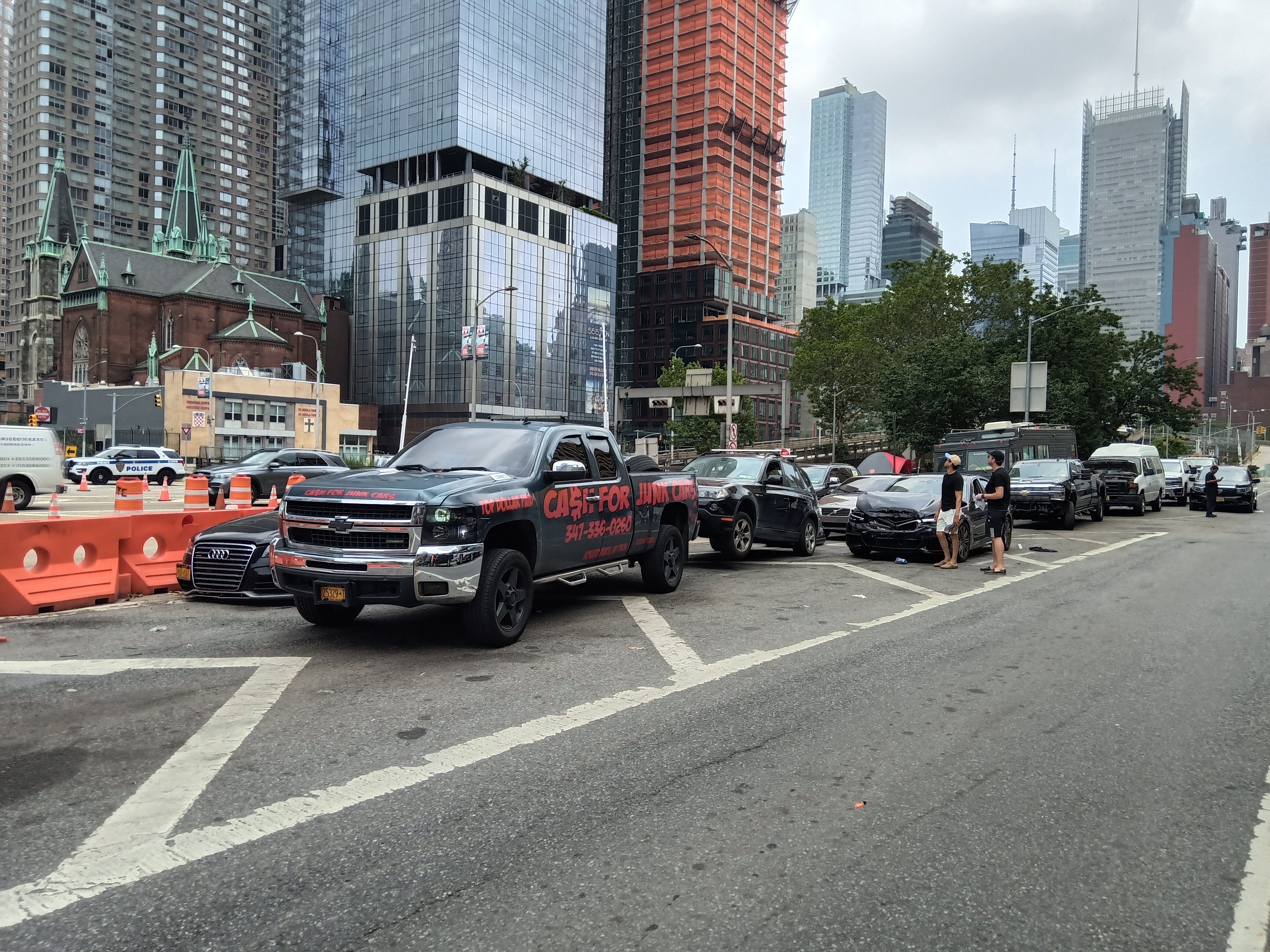 Cash For Junk Cars pickup truck parked on a Manhattan street with damaged vehicles nearby.
