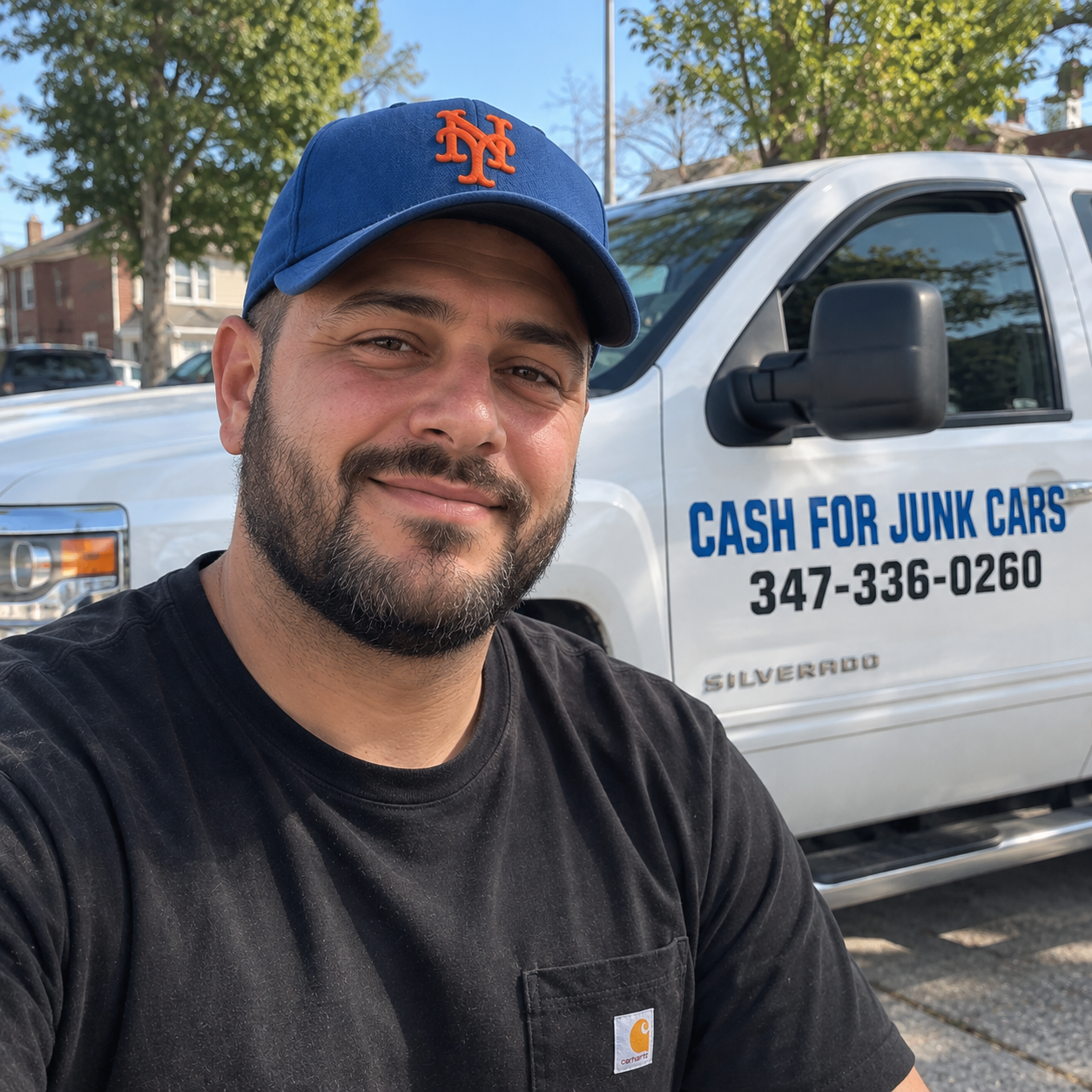 Smiling man wearing a blue baseball cap beside a Cash For Junk Cars truck.